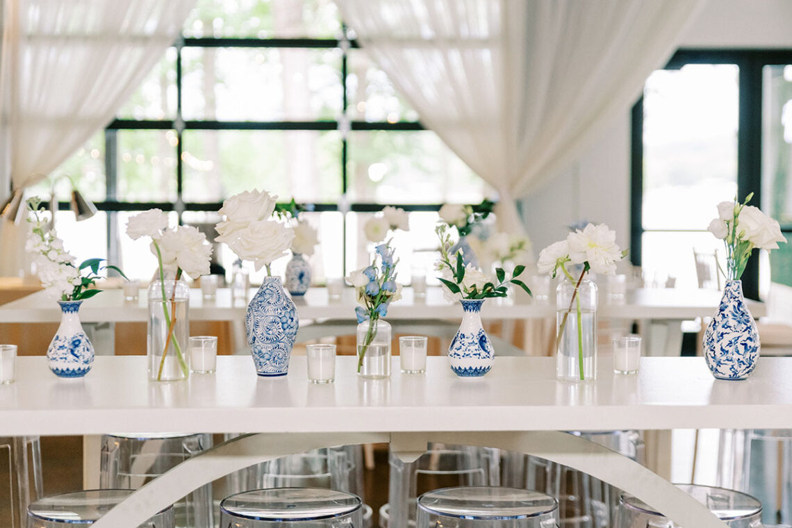 Close up of all white wedding reception tables with blue bud vases last summer