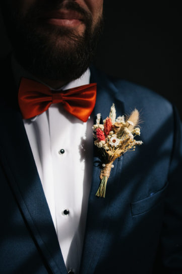 Fall inspired boutonniere on grooms navy suit with an orange bowtie