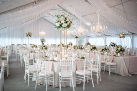 Sunset Terrace wedding reception with neutral linens, white chairs, crystal chandeliers, and romantic arrangements with pastel roses and white hydrangeas