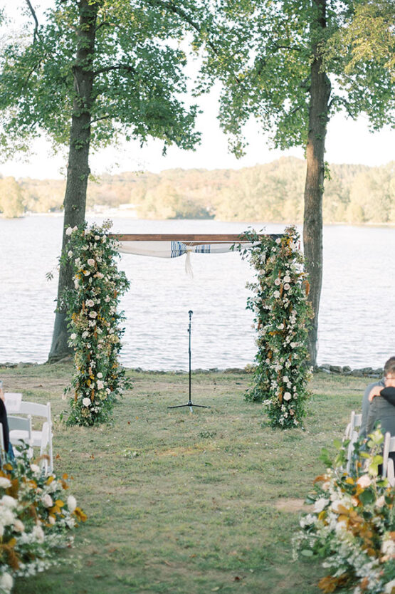 lakeside lawn ceremony with greenery decorated chuppah and aisle lined with florals