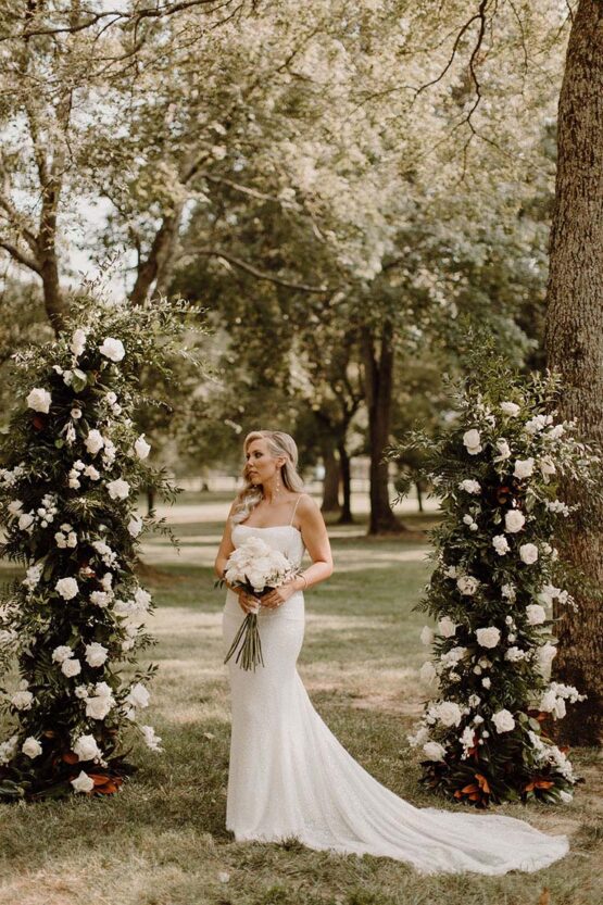 Brides poses between freestanding ceremony altar arrangements