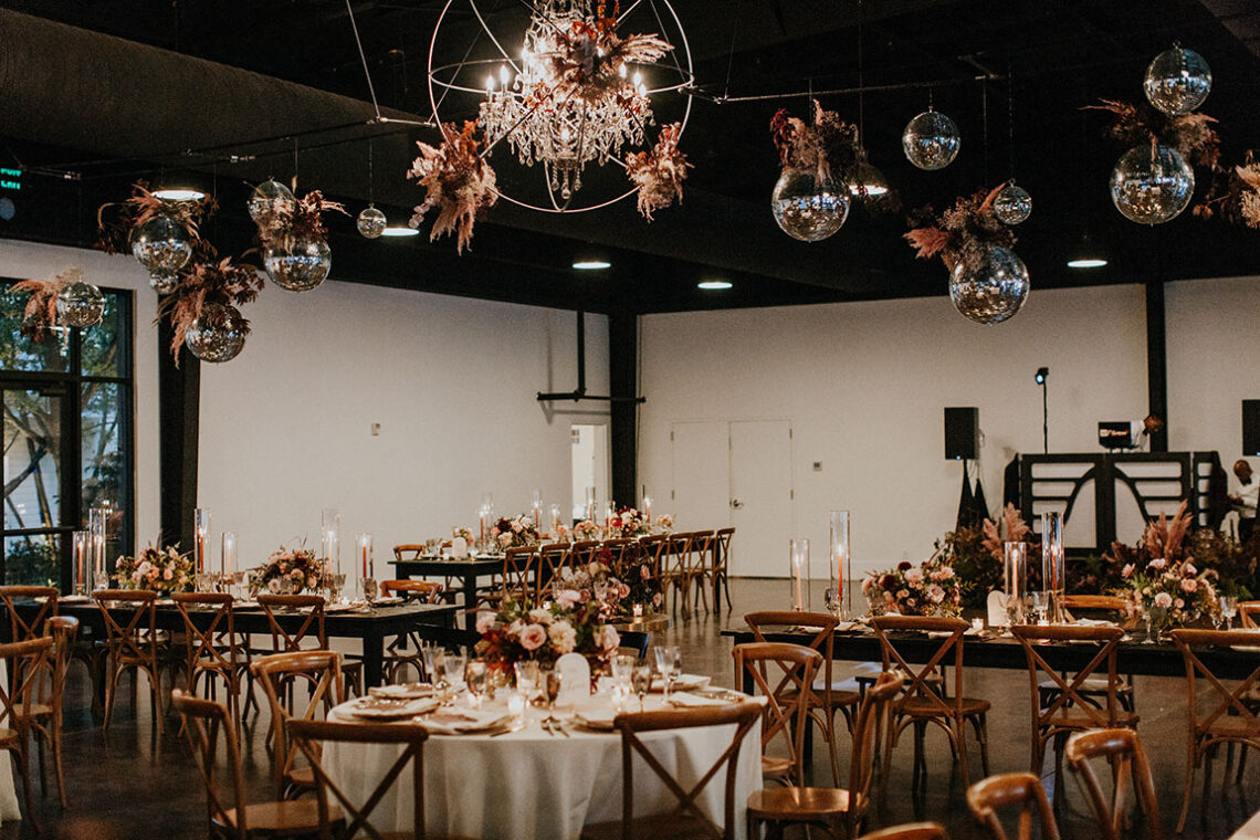 wedding reception set up with mixed seating and tables with disco balls and flower arrangements hanging from the ceiling