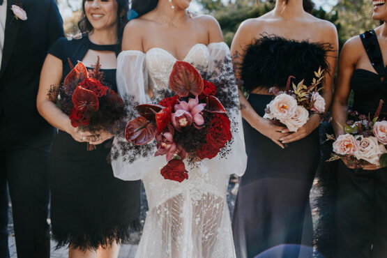 close-up of bride and bridemaids bouquets featuring bold red anthurium flowers, pastel pink roses, and moody greenery