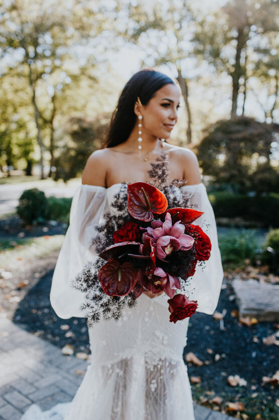 Trendy bride holding unique and bold bouquet of bright red anthurium flowers