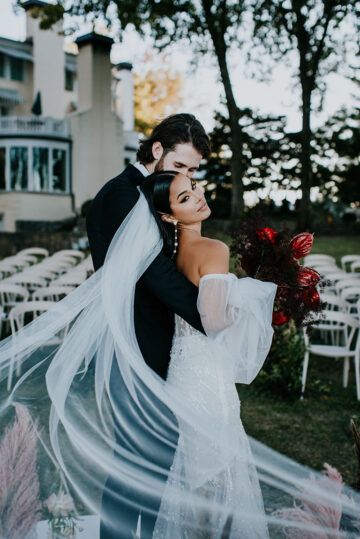 bride and groom embrace on lakeside lawn amid their ceremony setup