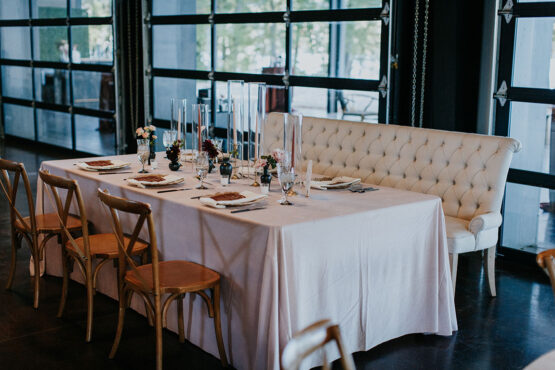 wedding reception table with mixed seating and white linens, decorated with taper candles in hurricane vases