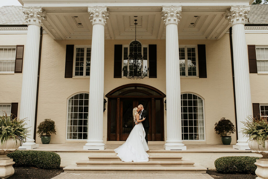 Bride and groom kiss on mansion's front steps