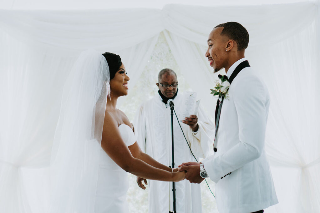 Danicia and Darin hold hands during wedding ceremony with officiant reading passage behind them