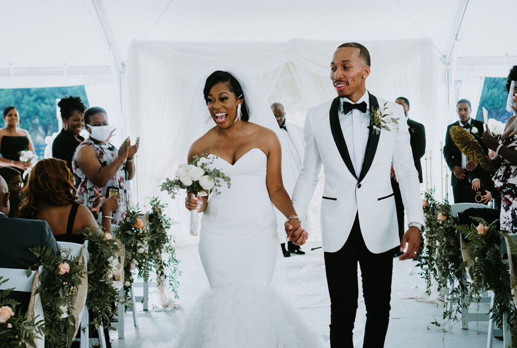 Danicia and Darin wedding recessional down their all-white aisle lined with greenery arrangements