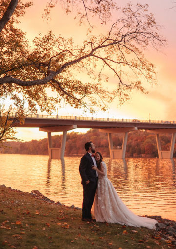 Bride and groom embrace on the lakeside as the sunset beams around them