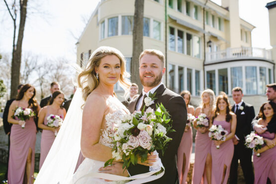 Wedding party portrait in front of The Estate at Cherokee Dock Large Wavy Bridal Hairdo with Spring Bouquet and Lace Wedding Dress