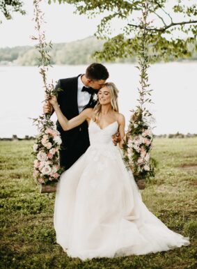 Bride and Groom Sitting on Swing on Lakeside Lawn