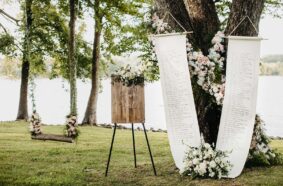 Summer Wedding Ceremony Seating Chart with elegant wooden sign and large scroll hanging from tree decorated with white and pink roses