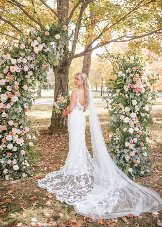bride poses in front of an asymmetrical greenery floral arch