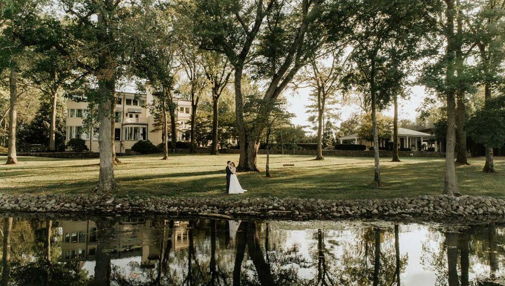 Bride and Groom Standing on Lakeside Lawn of luxury wedding venue with a view, pool, and accommodations