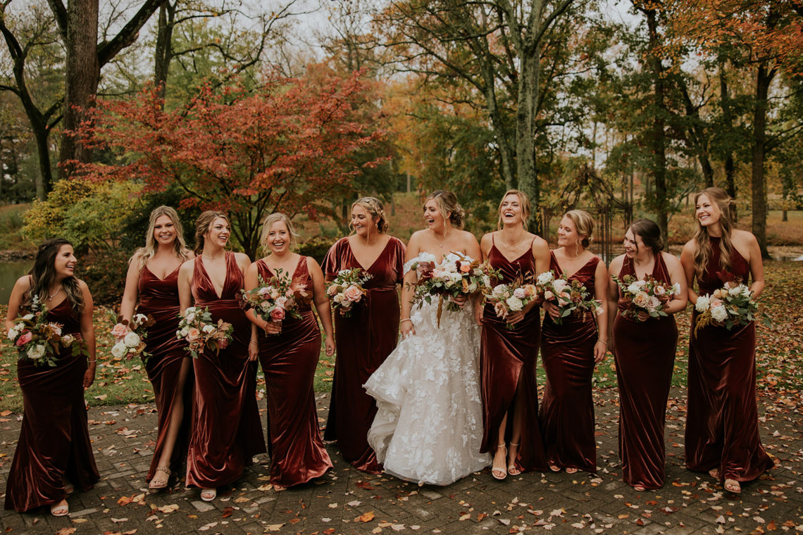 bridal party in velvet rust tones gowns walking through the fall foilage at the estate at cherokee dock