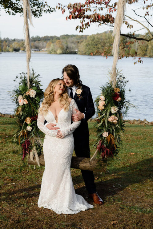 Gray and Billy pose on the swing decorated with greenery and flowers on our Lakeside Lawn