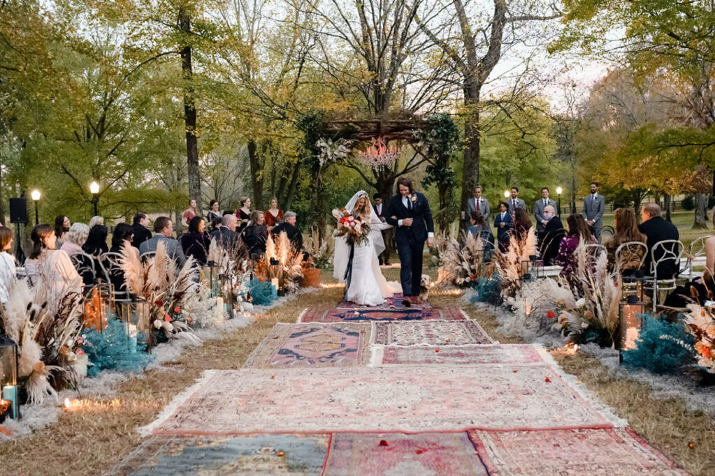 Gray and Billy's Wedding Recessional down ceremony aisle lined with oriental rugs, boho arrangements, and colorful dried florals