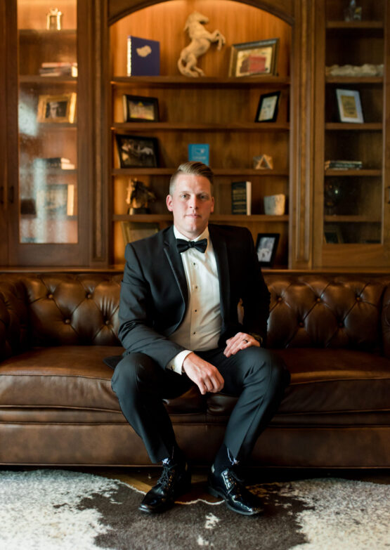 Groom wearing classic black tuxedo while posing in our mansion's library.