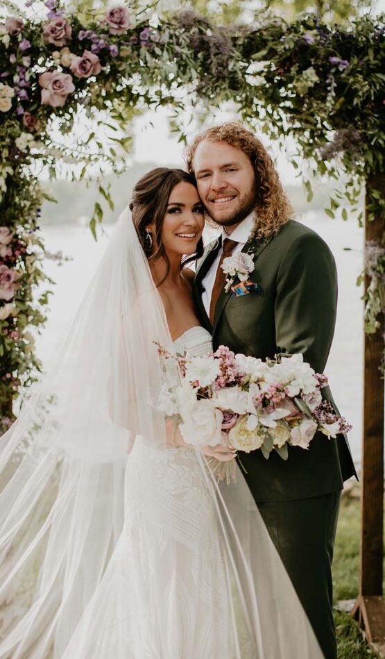 Hannah & Nick pose for a photo under their floral ceremony arch