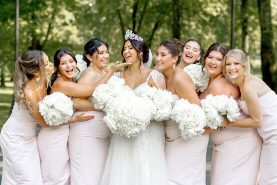 Bride in Lace Gown with Corset Bodice Matching Bridal Cape and Bejeweled Tiara with Classic Bun Updo and Face-Framing Curls | Full Round White bouquet