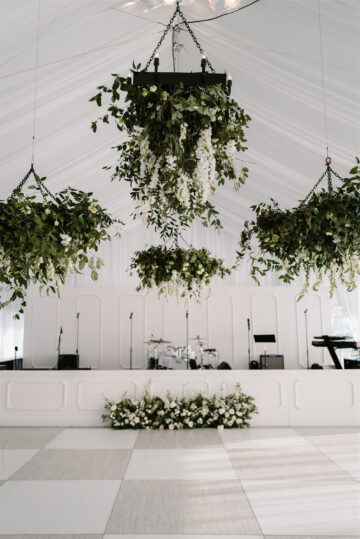 sunset terrace set with white draping a dance floor and custom stage along with hanging greenery installations and white lounge furniture set ups