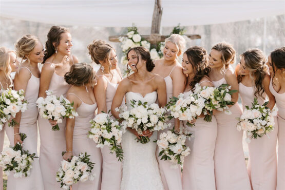 bridal party wearing light pink dresses with spaghetti straps all holding matching floral bouquets