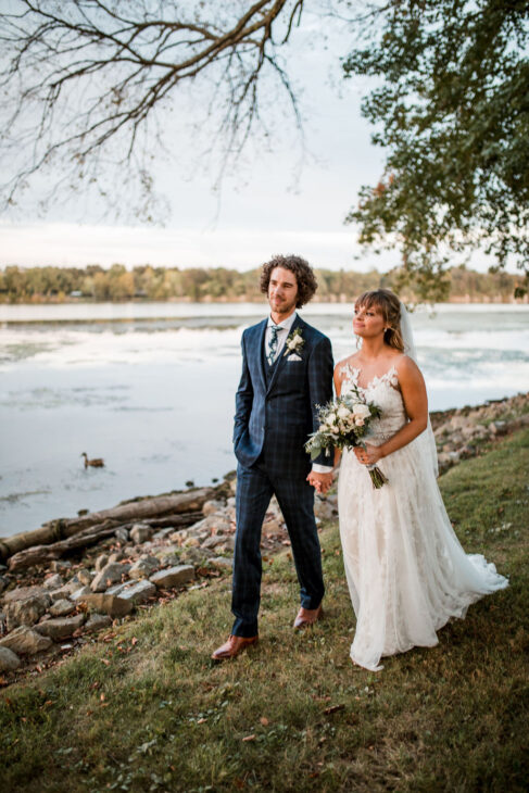 Bride and groom walk alongside lake