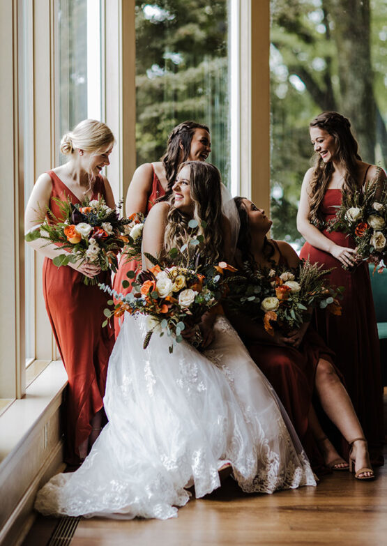 Bride and her bridesmaids their dresses were a gorgeous rust-colored sateen, elegantly accented by the fall-themed bouquets.