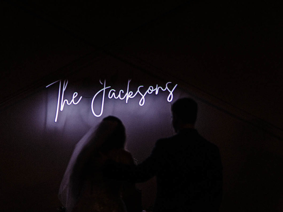 Bride and groom stand in front of bright custom neon LED sign