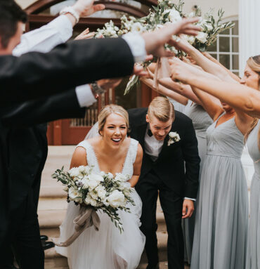 Laura and Mark walking under hands of wedding party and cheering