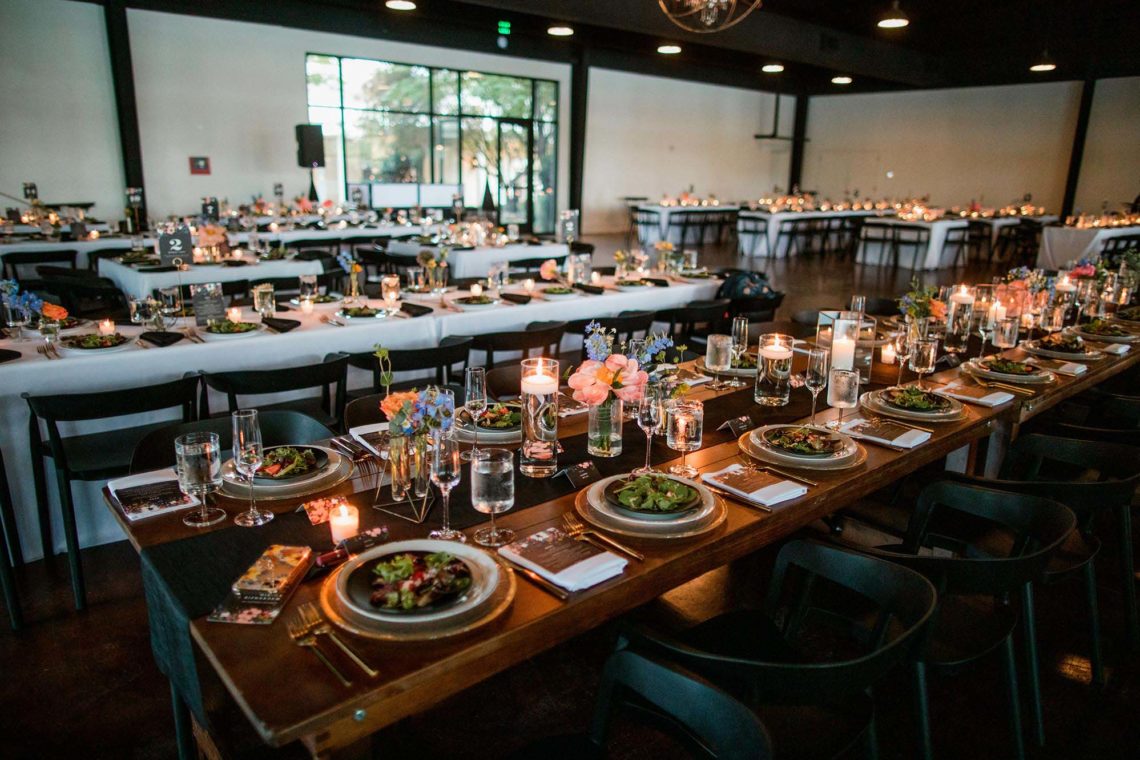 Dark wood wedding reception table with plated salads, small floral centerpieces, and candles