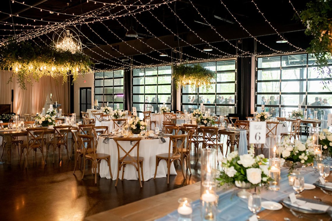 Hanging Greenery Installation with Edison Bulb Lighting with White Rose Centerpieces and Floor-to-Ceiling Drapery | Lakeview Event Center at the Estate at Cherokee Dock