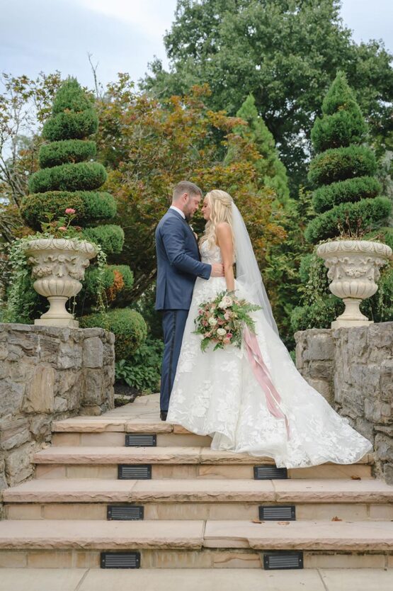 Groom in Navy Suit with Bride in Lace Wedding Dress and Long Veil with WIth Rose Bouquet