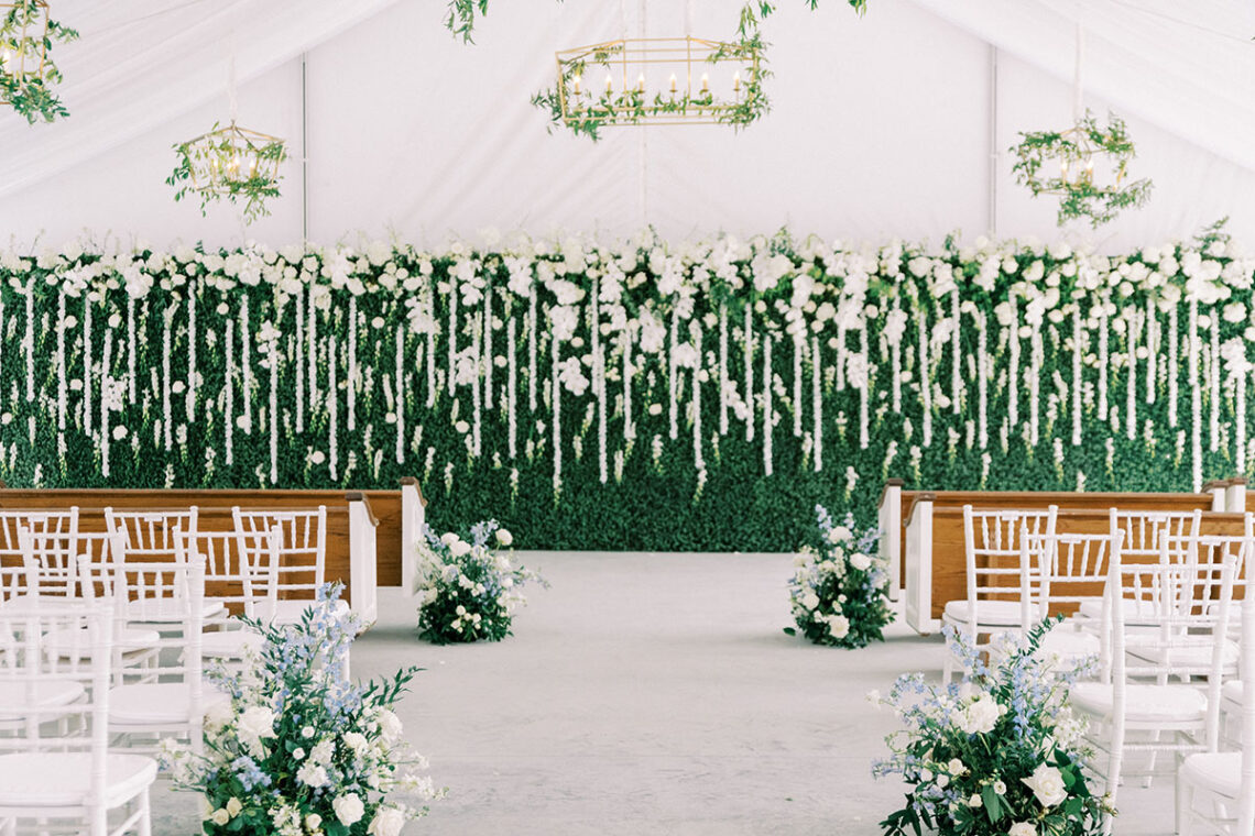 McKenna + Tres wedding ceremony setup with a greenery wall backdrop