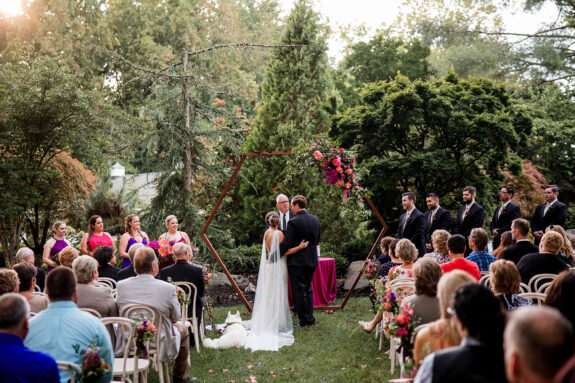 Wedding ceremony in Serenity Gardens with bride and groom in front of hexagonal arch with bold floral arrangement