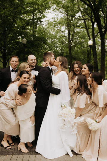 bride and groom embrace with wedding party around them