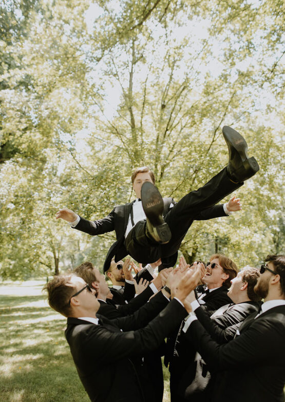 Groomsmen hoist the groom in the air and throw him up