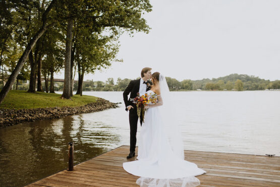 The groom kisses his bride's forehead on the dock at Cherokee Dock