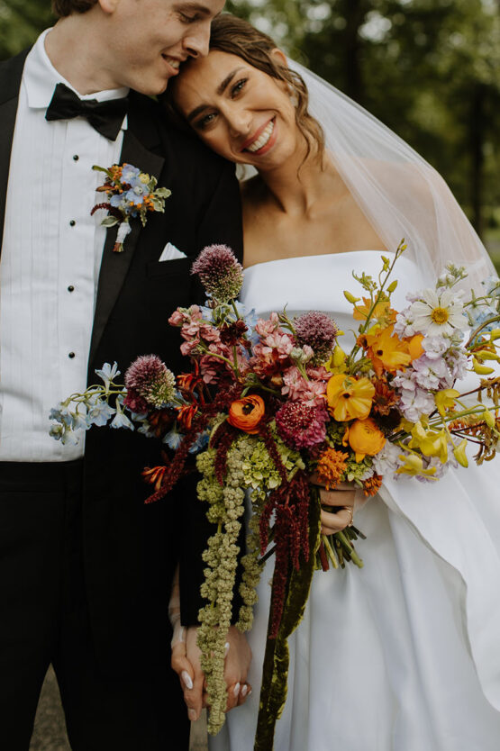 The bride holding a vibrant and whimsical bouquet as she leans her head on the groom's shoulder