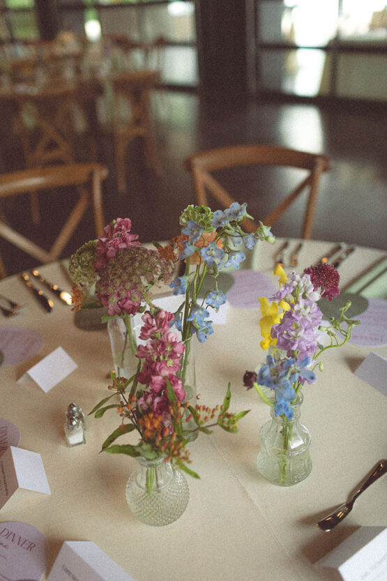Film photography of a round table's centerpieces of 4 small bud vases with various vibrant blooms