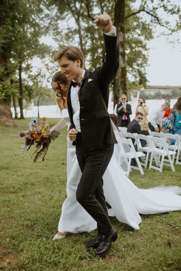 A groom fist bumps the air at the end of the ceremony aisle during the recessional