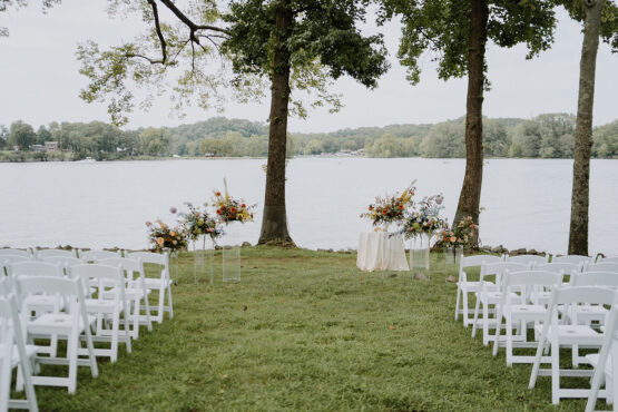 A wedding ceremony setup on the Lakeside Lawn with white chairs and glass podiums at the alter with vibrant whimsical arrangements on top