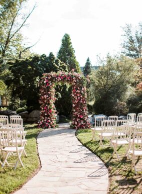 Ceremony arch covered in greenery and pink flowers in Serenity Gardens