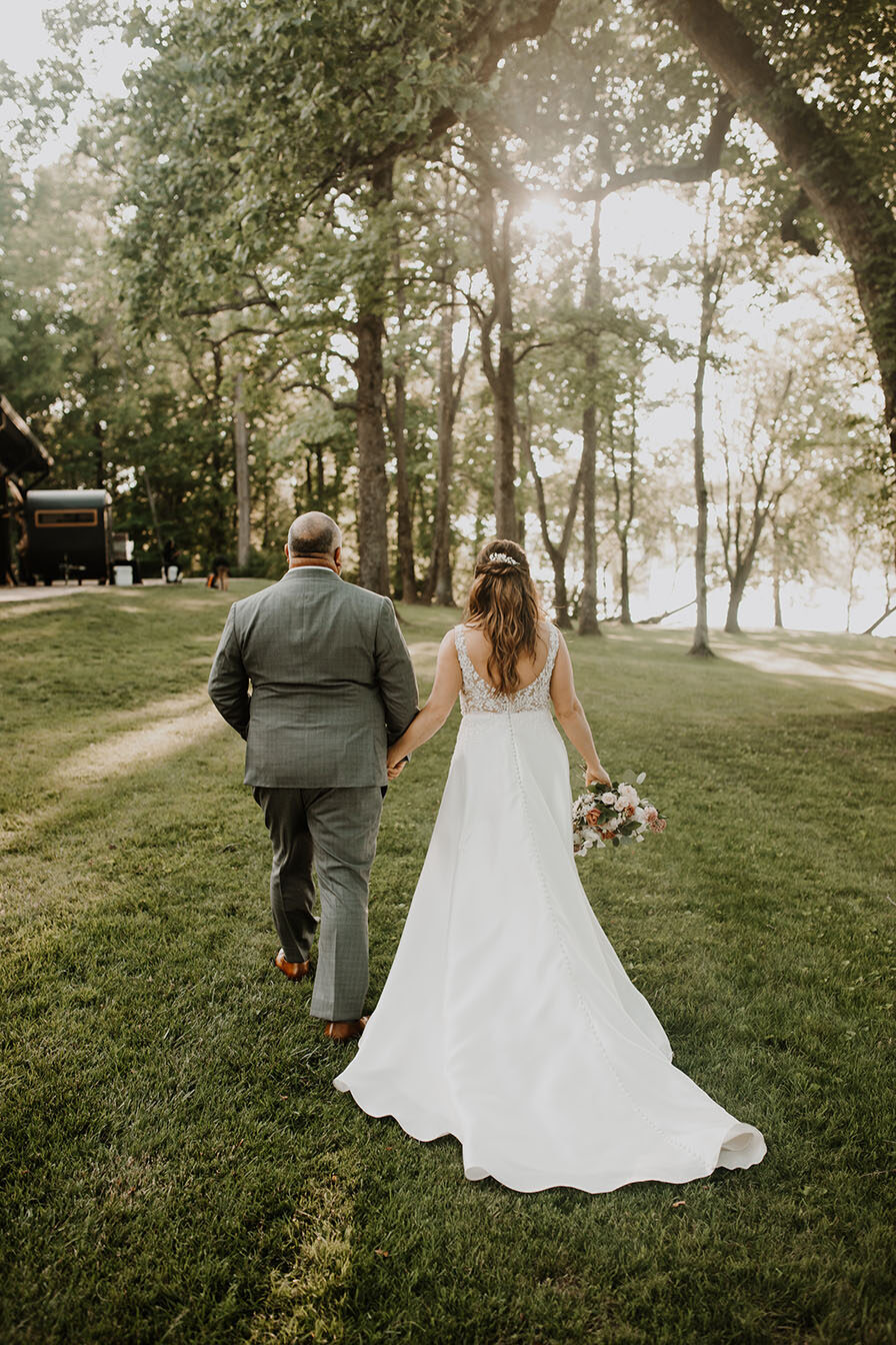 bride and groom walk hand and hand on the lakeside lawn