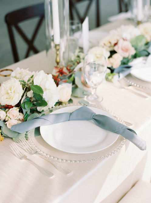 Wedding reception table place setting with blue napkins and white floral arrangements