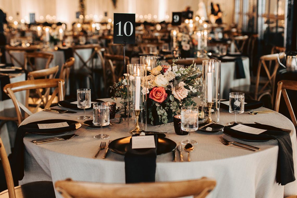 Wedding Reception Table Setting with black plates and napkins, taper candles, and romantic floral centerpiece